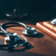A physician’s stethoscope resting on a walnut desk beside a leather journal